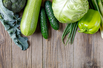 Border of green raw vegetables on wooden background. Top view of healthy organic food. Copy space