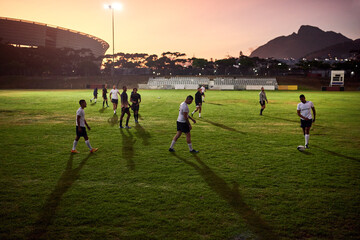 We never stop training. Full length shot of a diverse group of sportsmen playing rugby at dusk in a...
