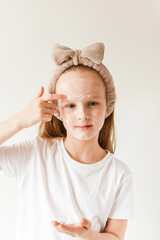 Young blond girl applying moisturizing cream on her face. Skin care and beauty concept