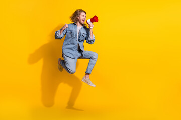 Fototapeta na wymiar Full length photo of cheerful confident guy dressed jeans shirt jumping shout toa emtpy space isolated yellow color background
