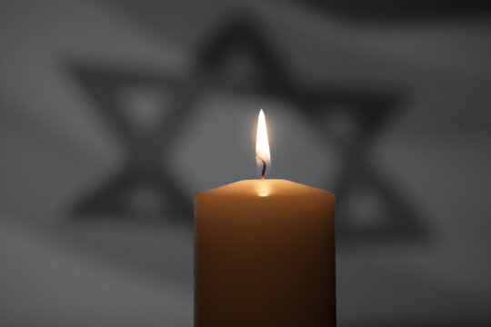 Burning candle on Israel flag background. International Holocaust Remembrance Day, January 27.