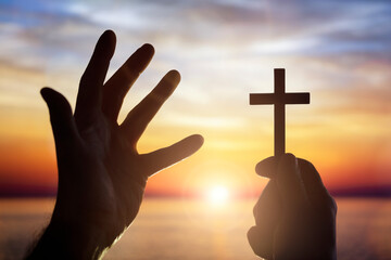 Holding up religious cross crucifix to sky across the sea at sunset background