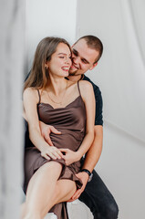 A man and a pregnant woman are sitting on a windowsill and hugging each other