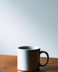 White coffee cup on a wooden table with a white wall in the background.