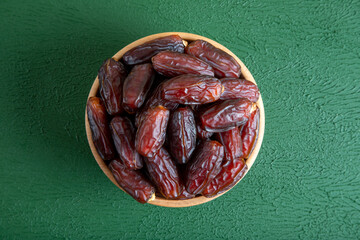 Date fruits in wooden bowl,on green background


