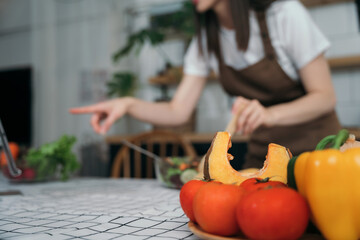 woman using laptop computer searching and learning for cooking healthy food from fresh vegetables and fruits in kitchen room.