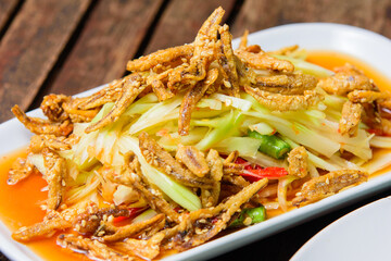 Spicy papaya salad with crispy fish on white dish.