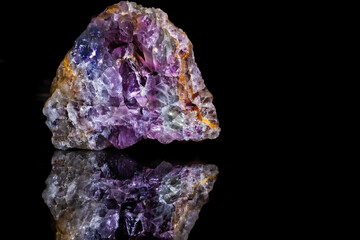 Amethyst mineral with crystals on a black background with reflection.