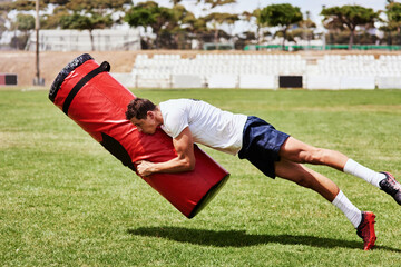 Tackle it like you mean it. a young rugby player training with a tackle bag on the playing field.