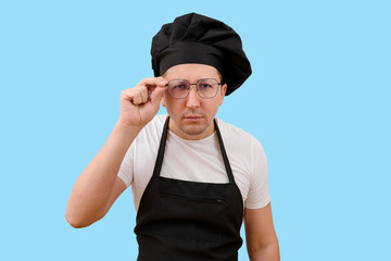Young male chef in cap and glasses looking at camera on blue background. Cooking and people concept