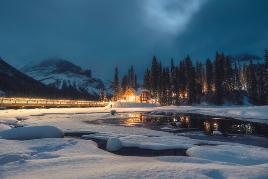 Frozen Emerald Lake with wooden lodge glowing in snowfall on winter at the night