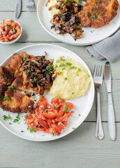Pork schnitzel with roasted onions, mashed potatoes and tomato salad on a plate