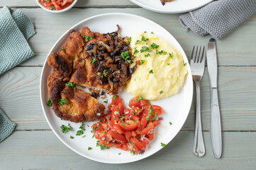 Plate with breaded pork schnitzel, fried onions, mashed potatoes and tomato salad