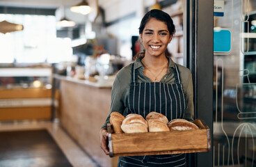 Served fresh just for you. a young woman holding a selection of freshly baked breads in her bakery.