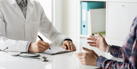 Doctor and patient talking in medical office at hospital. Closeup of doctor medical professional hands taking notes and writing prescription for patient during a consultation. Medicine and healthcare