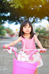 Portrait image of 5-6 years old kid. Happy Asian child girl ride a bike at the park outdoor. Exercise for health and sport. Summer season.