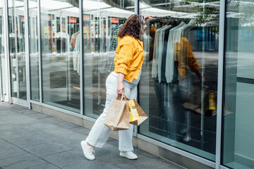 Plus Size Fashion and Trendy Plus Size Clothing, Plus-Size Fashion Tips with a Body-Positive Attitude. Happy curve plus size woman with shopping bag near shop windows