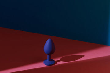 Blue buttplug sex toy on a colorful background. Photo of anal toy for adult with contrast shadows 