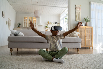 Digital child. Little African American boy kid playing VR simulation game, curious schoolboy exploring planets and stars in virtual and augmented reality, sitting on floor and touching air with palms