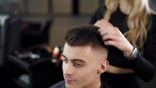 A barber woman styling short hair with the hands of a young man in a barber shop. moving camera