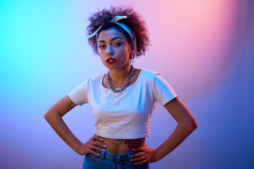 Portrait of cool Kazakh girl with curls and tattoo posing in neon light isolated on studio...