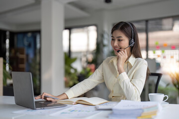 Fototapeta premium Portrait of happy smiling female customer support phone operator at workplace. Smiling beautiful Asian woman working in call center