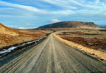Piste de sable et de gravier traversant l'Islande et donnant sur une montage enneigée et parsemé...