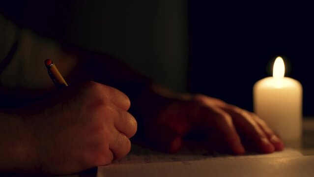 Cinematic man writing letter by single candlelight at night close up, unrecognizable male. Paperwork in retro style without electricity