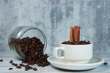 A cup full of coffee beans and cinnamon sticks.