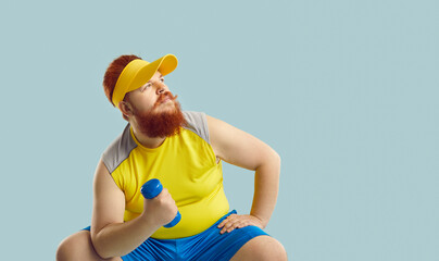Funny plump fat man with ginger beard, in yellow top sitting on blue studio background, holding...