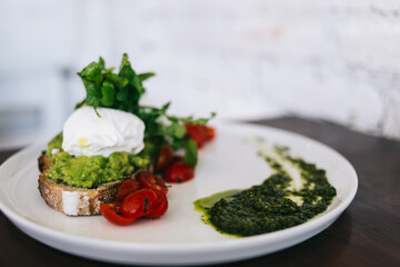 From above of plate of poached egg on bread with spinach leaves and tomatoes placed on table against white wall