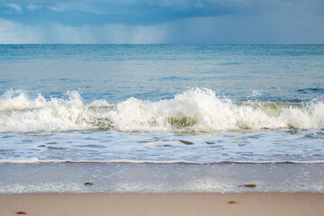 Sea waves crash on the sandy shore in bad weather. Small waves on the sandy beach.