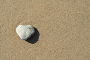 Fototapeta na wymiar A heart-shaped stone on the shore. Sandy beach with a light sea wave. Background to a pleasant holiday, relaxing vacation and hiking in an ecologically clean area. Template with empty space for text