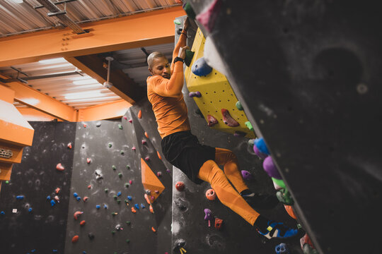 African American male rock climber clinging to bouldering wall
