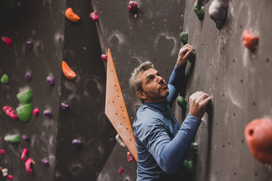 Mature male looking up with focus climbing a bouldering wall