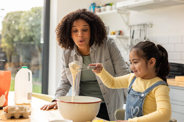 Mother helping daughter to bake at home in the kitchen
