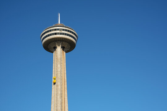 Looking up at observation deck and revolving restaurant pod of the Skylon Tower in Niagara Falls with one of the yellow elevator cars approaching the top.