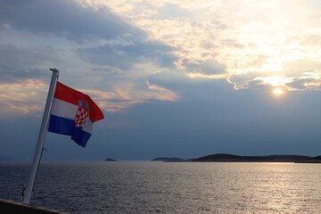 Flag of Croatia on the boat, blowing in the wind. Sea and sunset sky in the background. Selective focus.