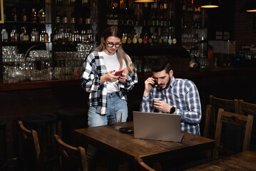 Two Diverse Entrepreneurs Have a Team Meeting in Their Stylish Coffee Shop. Barista and Cafe Owner Discuss Work Schedule and Menu on Mobile or Computer. Young Female and Male Restaurant Employees