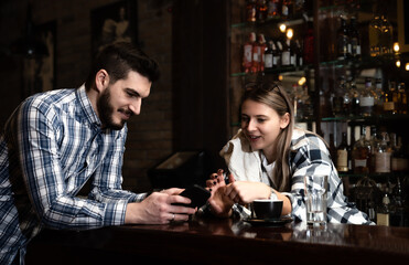 Two Diverse Entrepreneurs Have a Team Meeting in Their Stylish Coffee Shop. Barista and Cafe Owner Discuss Work Schedule and Menu on Mobile or Computer. Young Female and Male Restaurant Employees