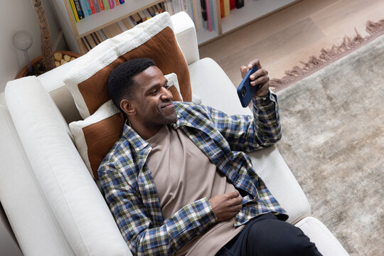 Overhead shot of African American male at home on sofa watching entertainment on a smartphone