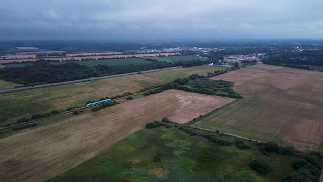 Aerial of a train passing by the wide green fields on a cloudy day in the background on Romo Denmark