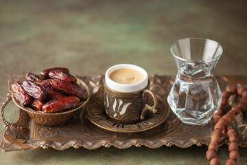 Cup of coffee and glass of water and dry dates on saucer ready to eat for iftar time. Islamic...