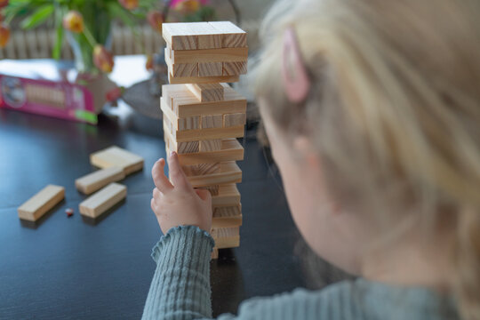 A toddler gitl builds a wooden tower on a table