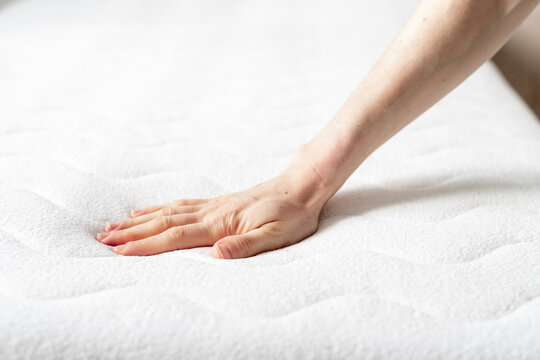 woman touching soft white mattress indoors, closeup