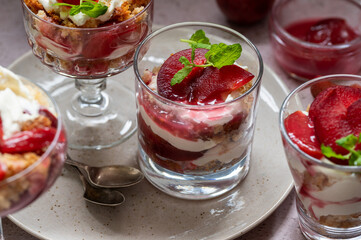 Trifles in layers with red plums and whipped cream in dessert, portioned glasses.