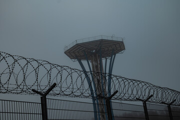 a tower in the fog. a tower in an airport. tower protected by a barbed wire enclosure
