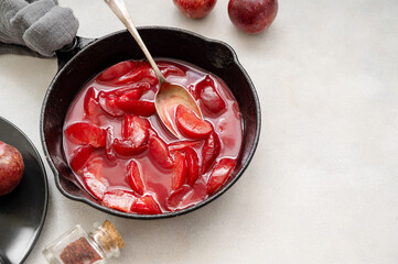 Red plums confiture or jam. Cooking fresh fruit sauce in black pan. Copy space.