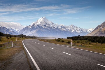 a long road surrounded by green trees and tall mountains near water