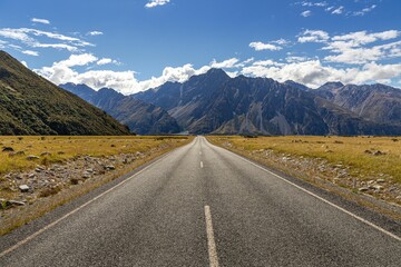 empty road in mountains and cloudy skies in new zealand, on a sunny day